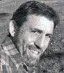 Black and white headshot photo of author KS looking over right shoulder with beard and plaid shirt